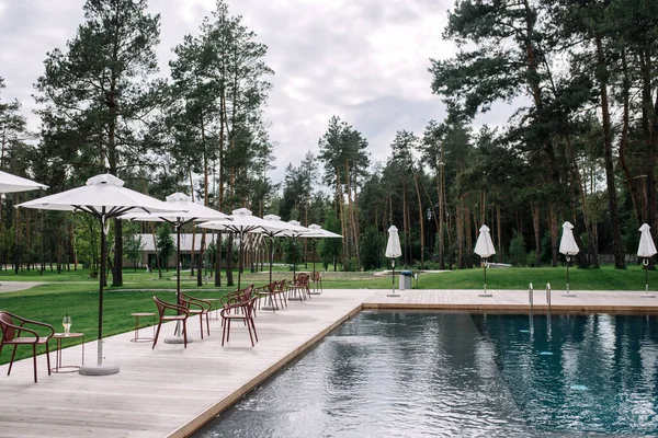 Wooden pool terrace with umbrellas. Recreation area outside the city. Outdoor pool in a country complex among pine trees.