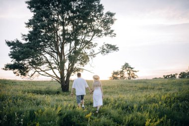 Tarladaki büyük, güzel bir ağacın yanında el sıkışan sevgi dolu bir çift. Yazın güzel doğa. Aşkın kavramsal fotoğrafı.