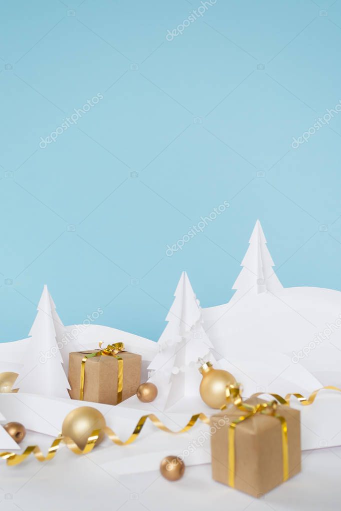 Fairy forest made of white paper with gold balls and gifts on blue background, Christmas holidays concept