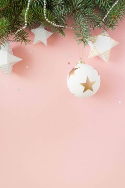 Mutlu Noeller ve mutlu yeni yıl. Noel kartı yeşil çam dalları ve soluk pembe bir arka plan üzerinde beyaz topu ile şenlikli.