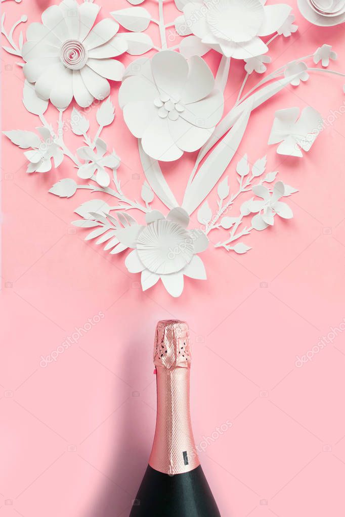 Champagne bottle with flower arrangement. Flowers, fragrance on pink background. Cut from paper