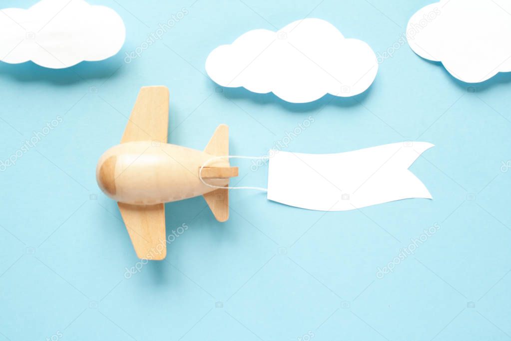 Children's wooden plane in the sky carries an empty banner. Clouds are cut from paper. Place your text.