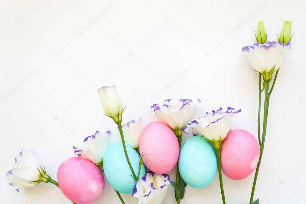 Beautiful white lisianthuses with colorful eggs on white background. Spring and Easter holiday concept with copy space.