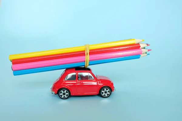 Um pequeno carro vermelho conduzido por lápis coloridos — Fotografia de Stock