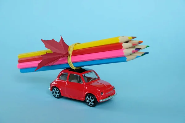 Um pequeno carro vermelho conduzido por lápis coloridos e uma folha de bordo — Fotografia de Stock