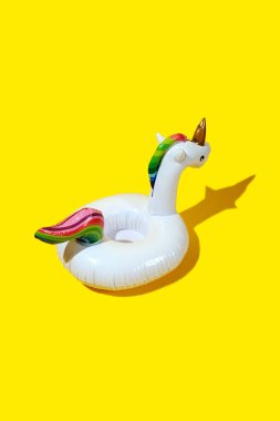 Kalın sarı arka planda şişme tek boynuzlu at havuz oyuncağı. Asgari yaz konsepti.