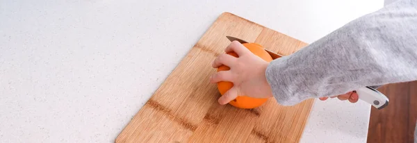 Jungenhände schneiden frische Orange in Küche — Stockfoto