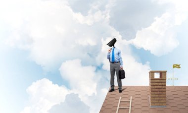 Evin çatısında baş durmak yerine kamerayla zum yapan yüzü olmayan bir iş adamı.