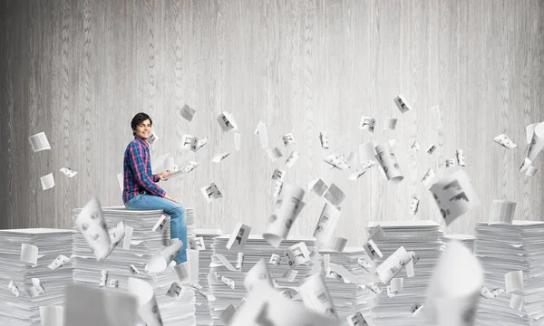 背景に灰色の壁に紙の文書を飛行中のカジュアル衣料品に座って若い男 ミクスト メディア — ストック写真