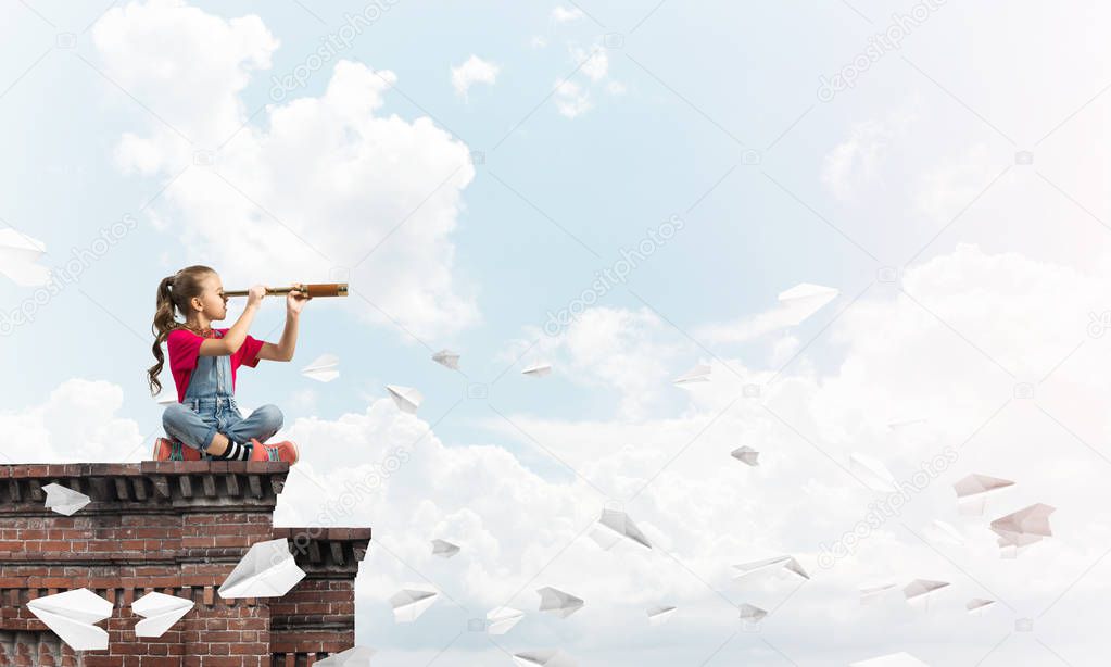 Cute kid girl sitting on house roof and looking in spyglass