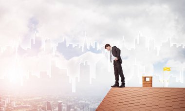 Genç işadamı tuğladan çatının kenarında dikilip aşağıya bakıyor. Karışık ortam