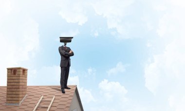 Evin çatısında baş durmak yerine kamerayla zum yapan yüzü olmayan bir iş adamı.