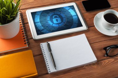 Ofis eşyalarıyla iş yeri ve ekranda asma kilit simgeleri olan tablet