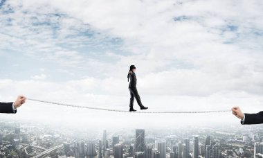 Gözlerinde perde olan bir iş adamı şehrin arka planında ipte yürüyor.