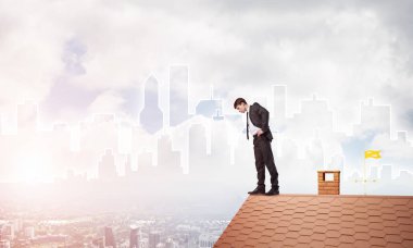 Genç işadamı tuğladan çatının kenarında dikilip aşağıya bakıyor. Karışık ortam