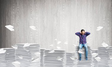 Arka plan gri duvar ile kağıt uçan arasında casual giyim oturan genç adam uçakları. Karışık teknik.