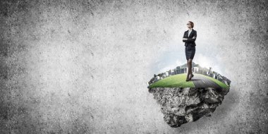 Yeşil yüzen adada beton zemine karşı duran kendine güvenen zarif bir iş kadını.