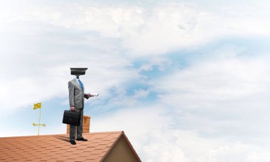 Evin çatısında baş durmak yerine kamerayla zum yapan yüzü olmayan bir iş adamı.