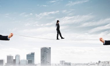 Gözlerinde perde olan bir iş adamı şehrin arka planında ipte yürüyor.
