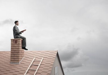 Elinde kırmızı kitap ile ev oturan takım elbiseli genç işadamı