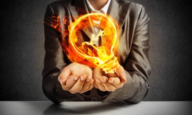 Resim işadamı elbiseli yanan ampul arka plan üzerinde koyu duvar ile onun ellerinde sunma kırpılmış.