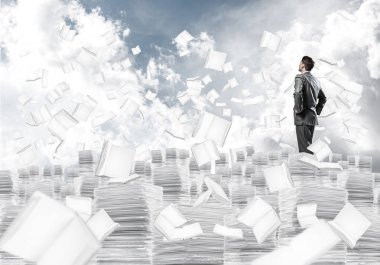 Kendine güvenen işadamı belgeleri kitap Clear sky ile arka plan üzerinde uçan arasında yığını üzerinde takım elbise ayakta. Karışık teknik.