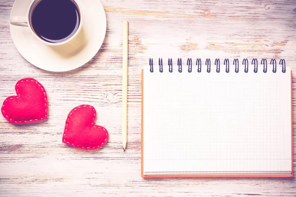 Coffee cup notepad pencil and two red hearts on wooden surface