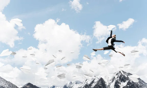 Attractive business woman in suit jumping in the air among flying paper planes as symbol of active life position. Skyscape and nature view on background. 3D rendering.