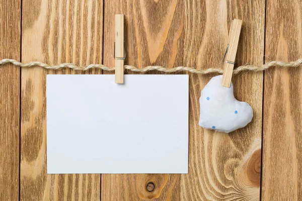 Blank sheet of paper hand made heart pinned to rope on wooden background