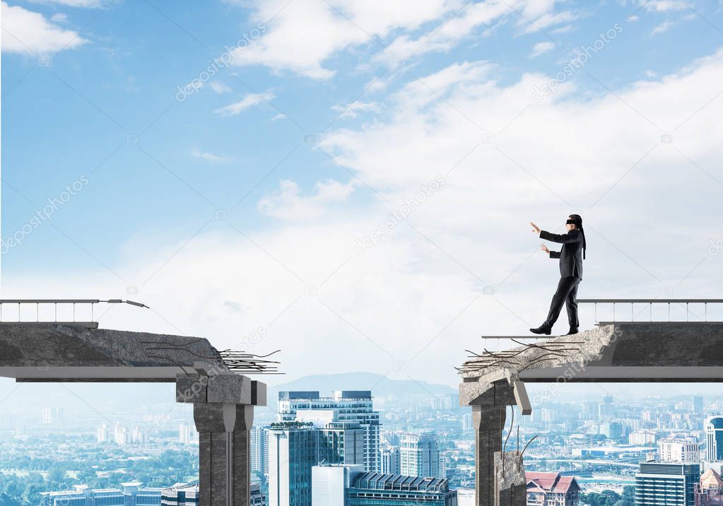 Businessman walking blindfolded on concrete bridge with huge gap as symbol of hidden threats and risks. Cityscape view on background. 3D rendering.