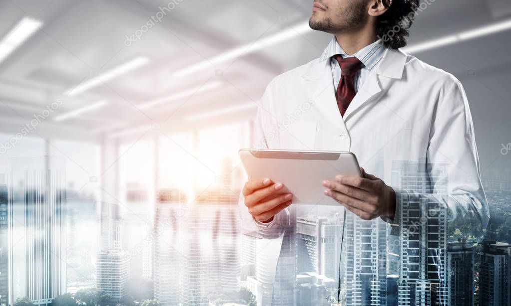 Double exposure of confident doctor in white sterile coat standing inside hospital office and modern cityscape view on background. Concept of modern medical industry