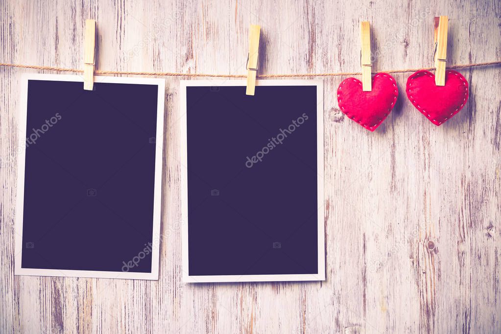 Instant photo frame and love hearts pinned to rope on wooden textured background