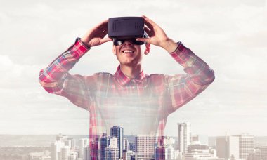 Sanal gerçeklik kulaklığı olan genç bir adam ya da şehrin arka planında 3 boyutlu gözlüklü.