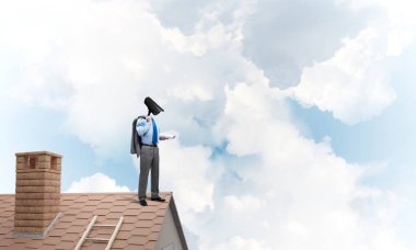 Evin çatısında baş durmak yerine kamerayla zum yapan yüzü olmayan bir iş adamı.