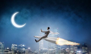 Arka plan üzerinde moon ile gece cityscape ve mavi karanlık gökyüzü ile roket üzerinde uçan takım elbiseli genç işadamı kavramsal görüntü.