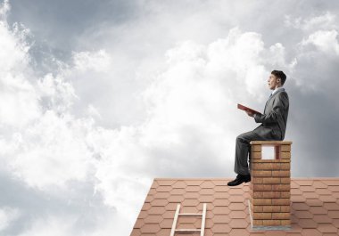 Elinde kırmızı kitap ile ev oturan takım elbiseli genç işadamı