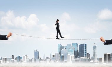 Gözlerinde perde olan bir iş adamı şehrin arka planında ipte yürüyor.