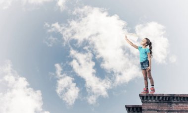 Binanın tepesinde kağıt uçakla oynayan sevimli, mutlu bir kız.