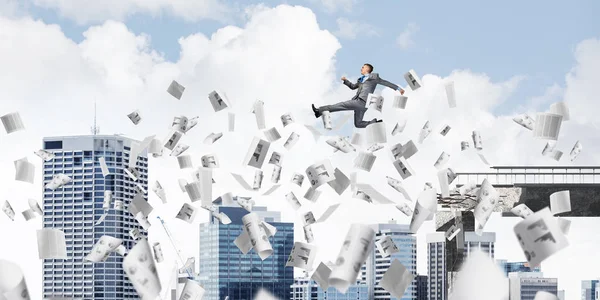Businessman jumping over gap with flying paper documents in concrete bridge as symbol of overcoming challenges. Cityscape on background. 3D rendering.