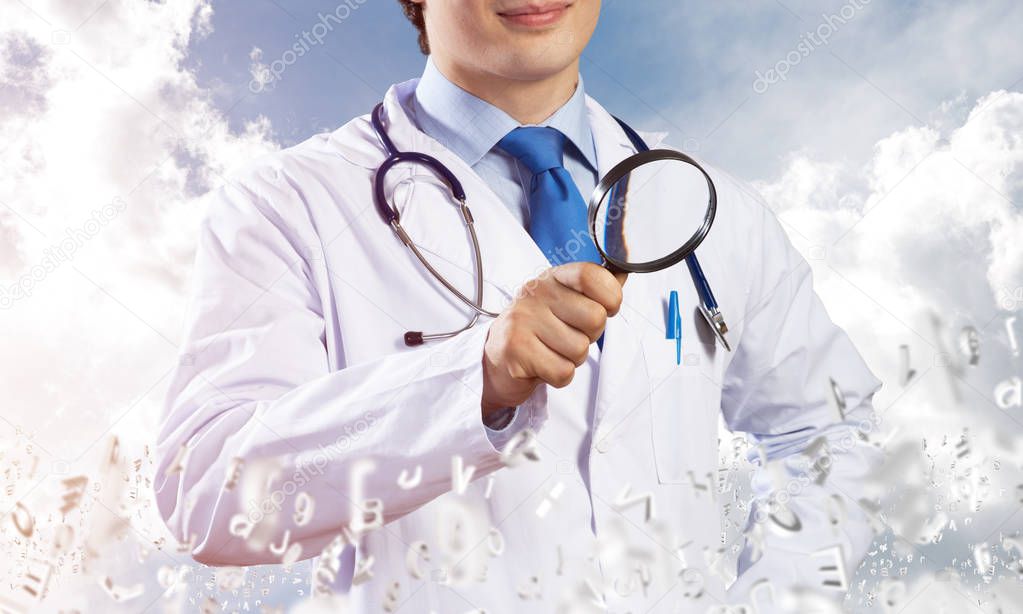 Cropped image of cheerful young doctor in white medical uniform holding magnifying glass in hand while standing among flying letters and cloudy skyscape on background