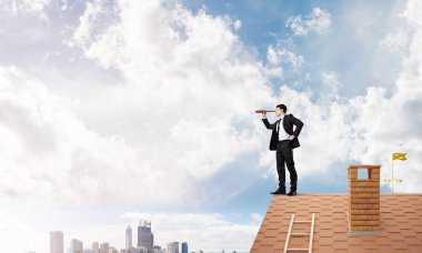 Genç kararlı işadamı çatının tepesinde dikilip dürbüne bakıyor. Karışık ortam