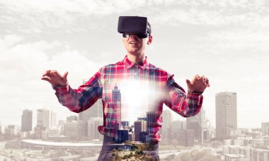 Sanal gerçeklik kulaklığı olan genç bir adam ya da şehrin arka planında 3 boyutlu gözlüklü.