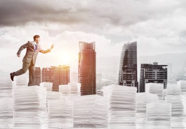 İş telefonu el ile güneş ışığı ve arka plan üzerinde cityscape belgelerle yığını üzerinde çalışan takım elbiseli adamı. Karışık teknik.