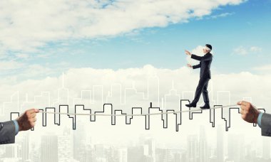 Gözlerinde perde olan bir iş adamı şehrin arka planında ipte yürüyor.