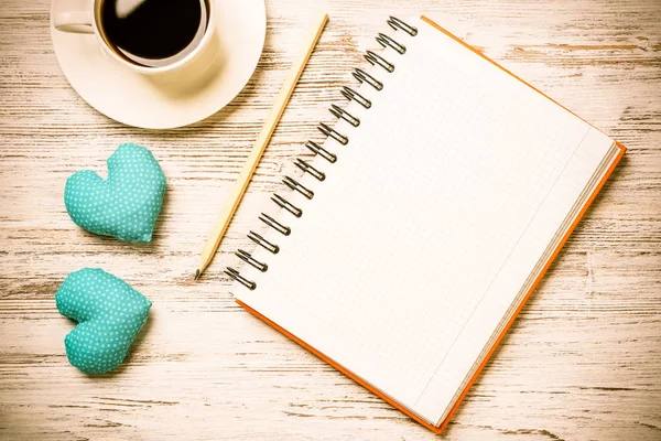 Coffee cup notepad pencil and two hearts on wooden surface