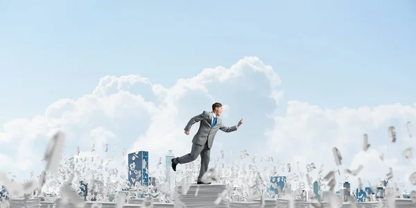 Businessman in suit running with phone in hand among flying letters with cloudly sky on background. Mixed media.