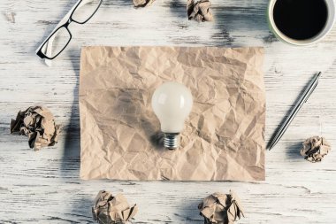 Sayfası, buruşuk Kağıt topları ve ahşap masanın üzerine yerleştirilen kahve buruşuk parçasına üstten görünüm ampul ile modern yaratıcı çalışma alanı'nın. En iyi fikir bulgusu kavramı.