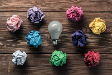 Birden çok renkli crampled kağıt topu ve ampul aralarında, yeni fikirlerden arama aracı olarak ahşap masanın üzerine yerleştirilen.