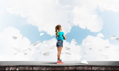 Sevimli kız etrafında uçan çatı ve kağıt uçaklar binasında ayakta