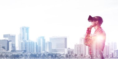 Sanal gerçeklik kulaklığı olan genç bir adam ya da şehrin arka planında 3 boyutlu gözlüklü.